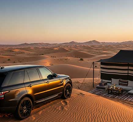 A luxury SUV parked on a sand dune at sunset beside a stylish desert camp tent, overlooking vast rolling dunes under a soft golden sky.