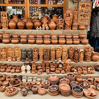 Display of traditional handmade clay pots, bowls, and carved figurines arranged on stone steps at a heritage market.